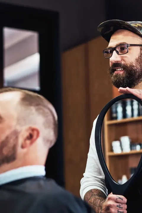 Barbero y cliente conversando sobre el corte frente al espejo