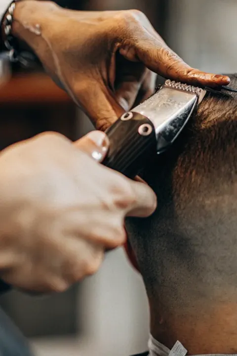 Barbero trabajando con la máquina en las patillas de un cliente