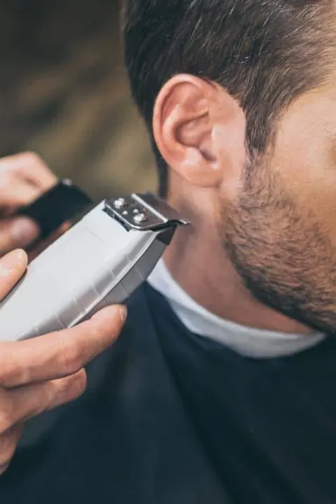 Mantenimiento del taper fade Barbero detallando las patillas con trimmer durante un retoque