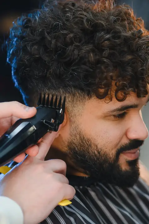 Barbero cortando el pelo rizado de un cliente con tijeras