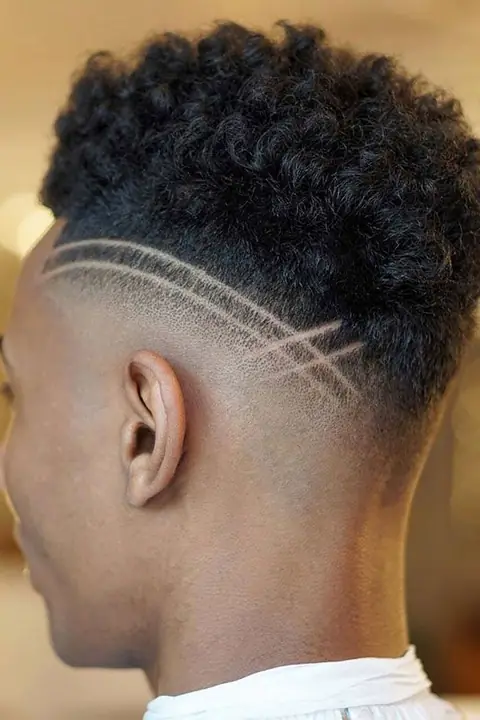 Taper fade rizado con doble línea curva diseñada en el lateral