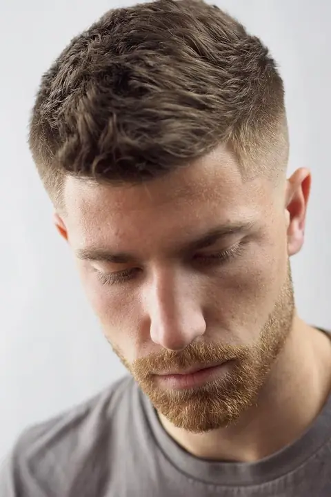 Taper fade clásico con textura natural arriba, vista de frente