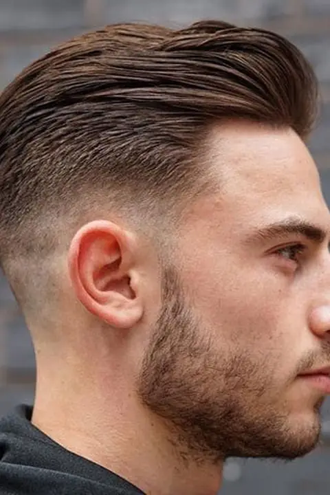 Low taper fade de perfil con tupé peinado y barba recortada